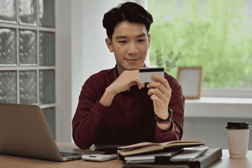 Uomo seduto alla scrivania con carta di credito in mano mentre controlla le informazioni del conto, immagine legata a chargeback e disconoscimento di un addebito sulla carta di credito.