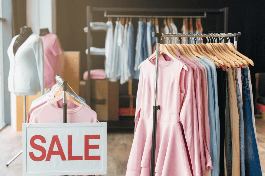Negozio di abbigliamento con cartello “SALE” e capi in esposizione
