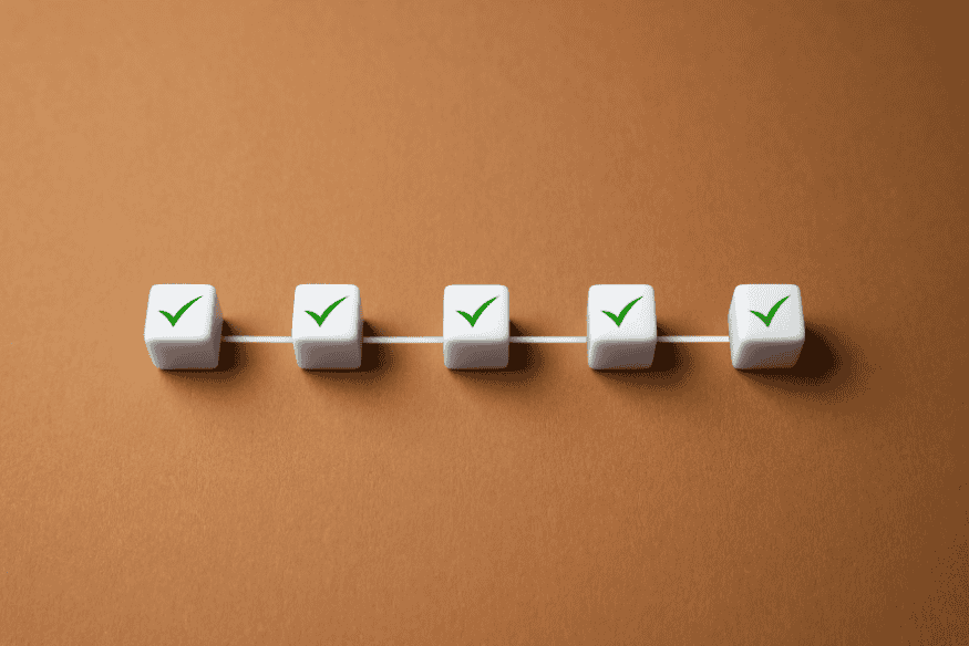 Cinque cubi bianchi con segni di spunta verdi su sfondo marrone che rappresentano il completamento di passaggi contrattuali.