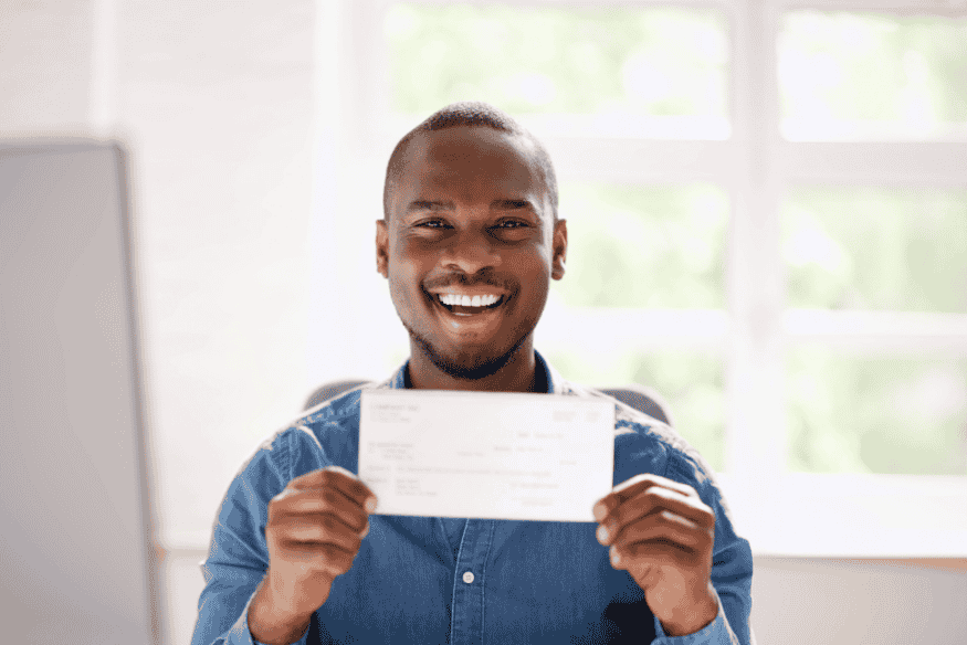 Persona sorridente che mostra un assegno, simbolo del primo stipendio e della gestione delle finanze personali.