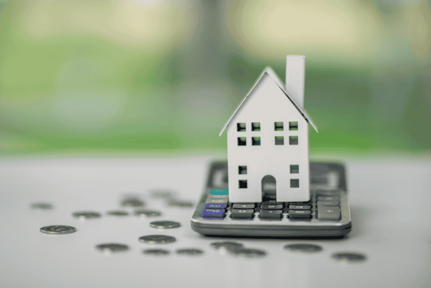 Modellino di una casa appoggiato su una calcolatrice con monete sparse sul tavolo
