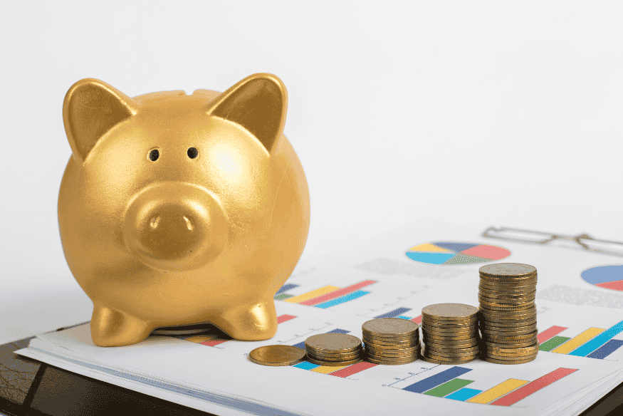 Salvadanaio dorato accanto a pile di monete su grafici finanziari colorati.