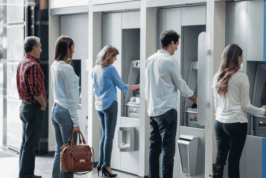 Persone in fila agli sportelli bancomat: perché il risparmio automatico aiuta a evitare prelievi e spese impulsive.